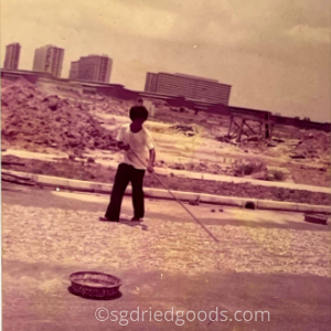 Man Drying Small Fish on Road in 1970s with New HDB in Background