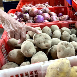 Potato and onion in shop, customer finger touching potato